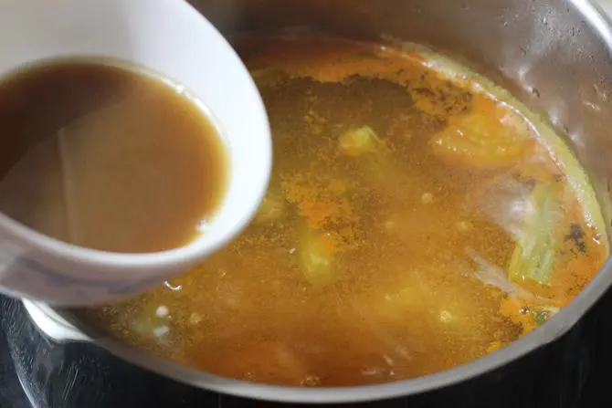 filtering tamarind juice to the pot of veggies for making sambhar