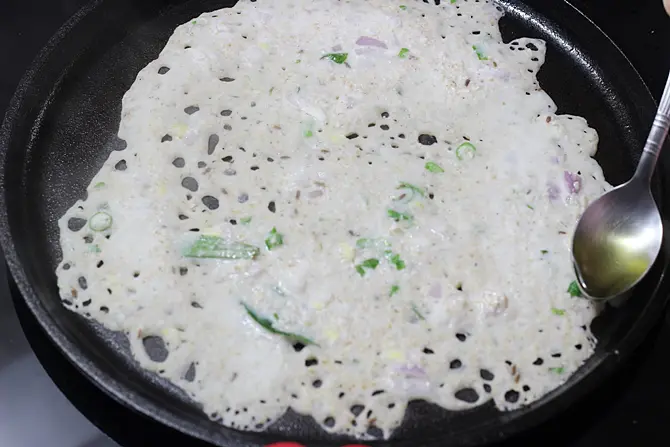 pouring oil around the edges to cook oats dosa