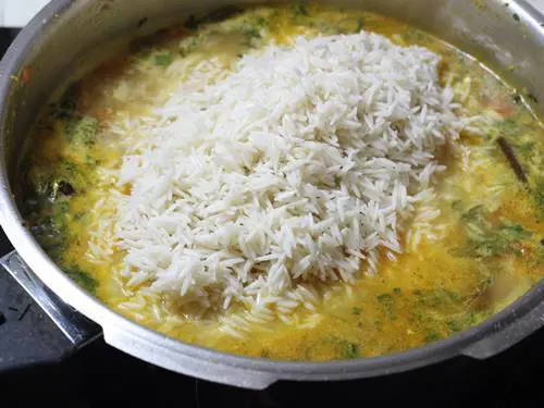 adding rice to boiling water to make chicken pulao