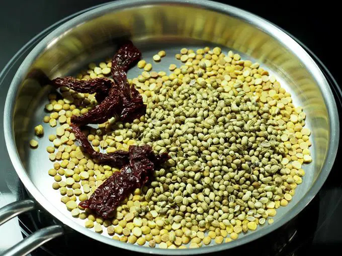 adding red chilies coriander seeds to make rasam powder