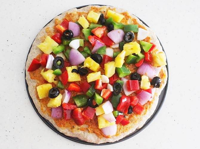 spreading chopped veggies for veg pizza recipe