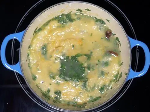 pouring water to bring dal palak to consistency