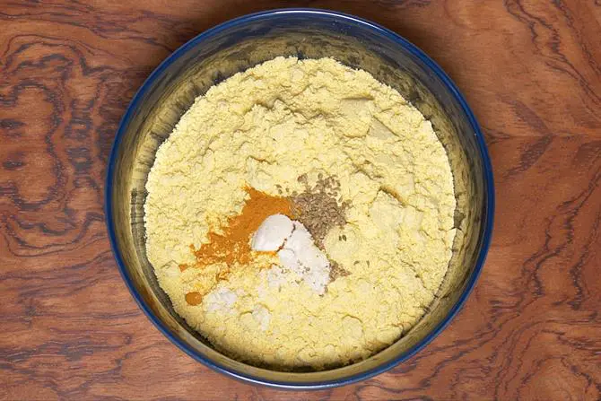 adding flour, salt spices to bowl to make besan chilla
