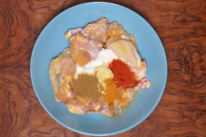 adding spice powders to marinate chicken for korma