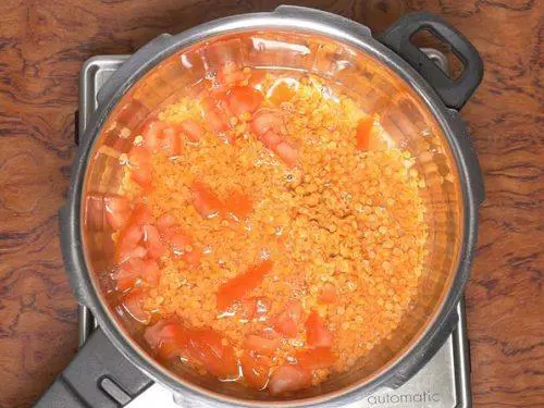 adding dal tomatoes to pot to make masoor dal
