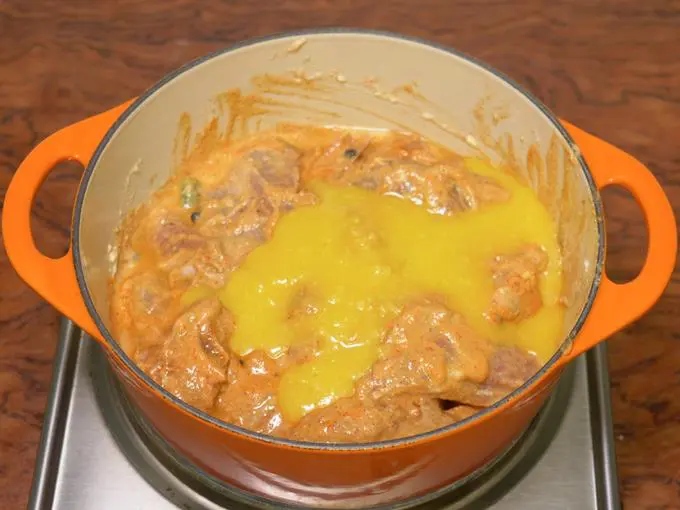 adding ghee to cook mutton korma
