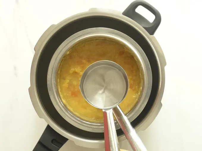 pouring water to bring tomato dal to consistency