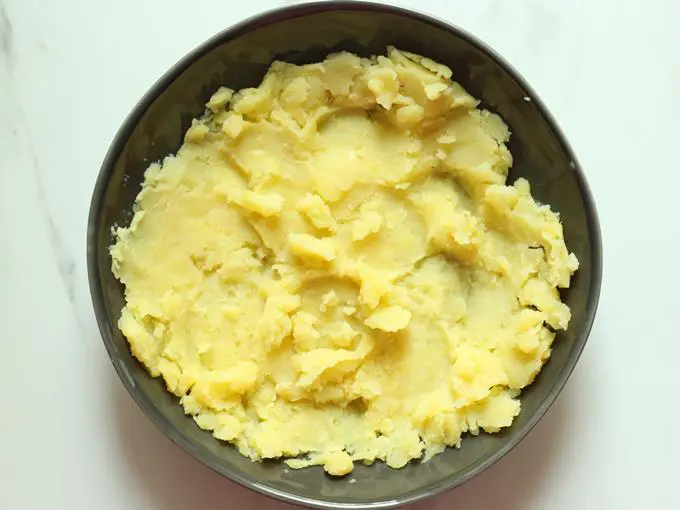 adding mashed potatoes to a bowl for cheese ball recipe