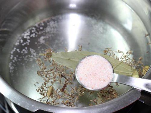 adding salt and spices to pot for rice