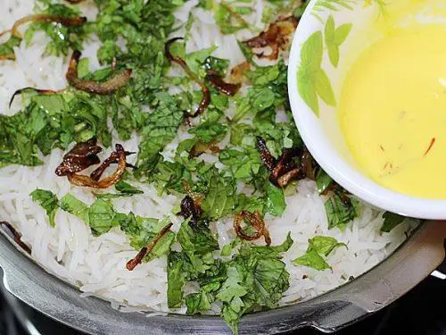 pouring saffron milk over layered rice