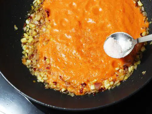 adding tomato puree to make red sauce pasta