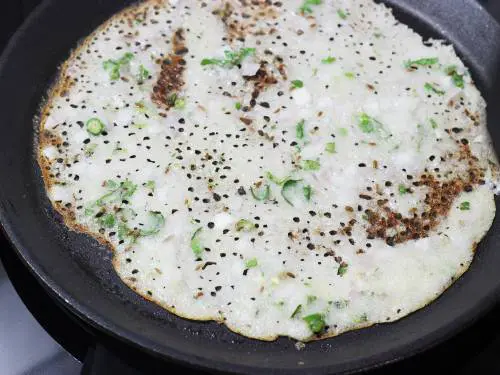 rava dosa batter toasting on a tawa