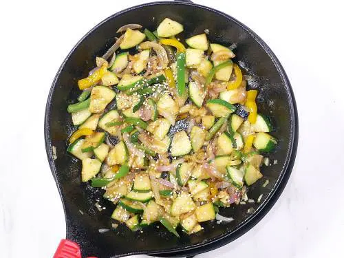 adding black pepper and sesame to stir fried zucchini