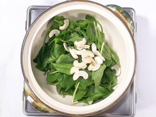 sauteing palak and cashews in a pot