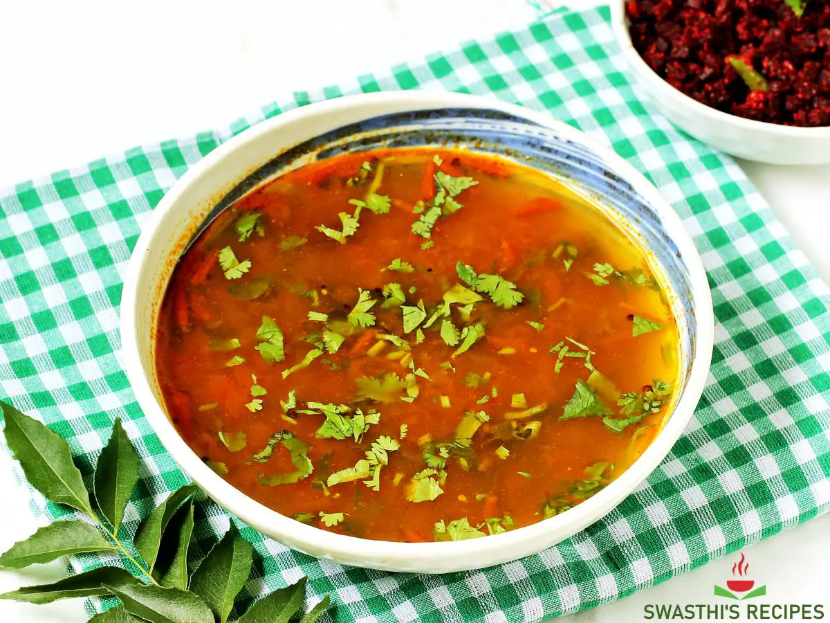 Rasam served in a white bowl with poriyal on the side