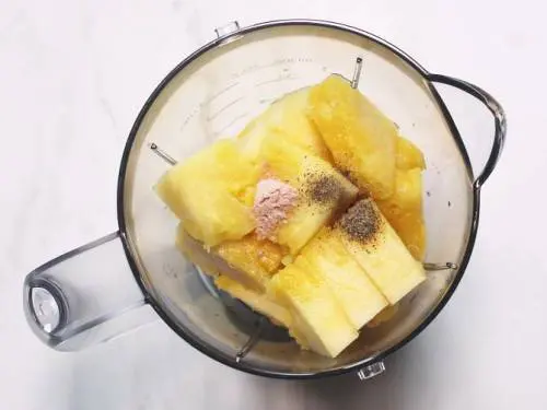 adding pineapple salt spices to a blender to juice