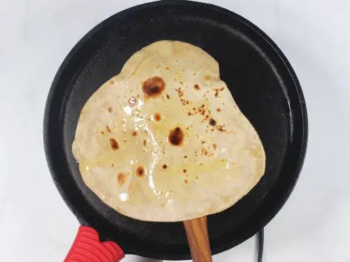 adding ghee to chapati while cooking