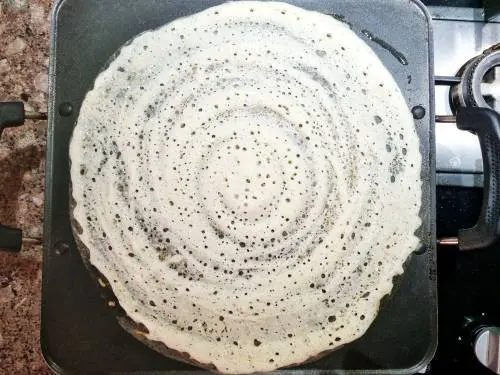 spread brown rice dosa batter on a pan