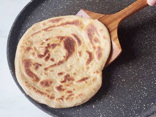 round flaky paratha on a pan